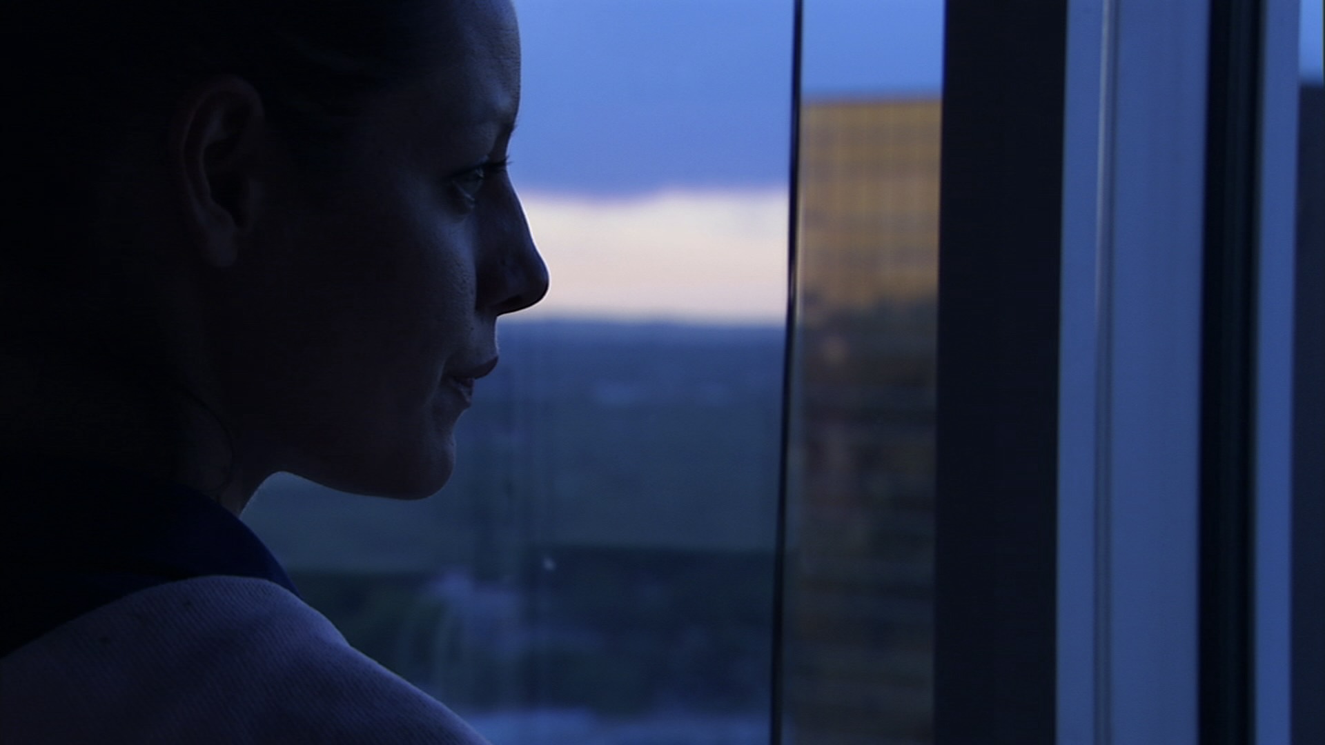 Maya Batten-Young as Roz in the film "River" looks out the window of a high rise office building. 